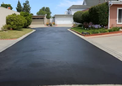 A driveway by Jones Asphalt VA features expert asphalt services, complemented by a house surrounded with trees and bushes.