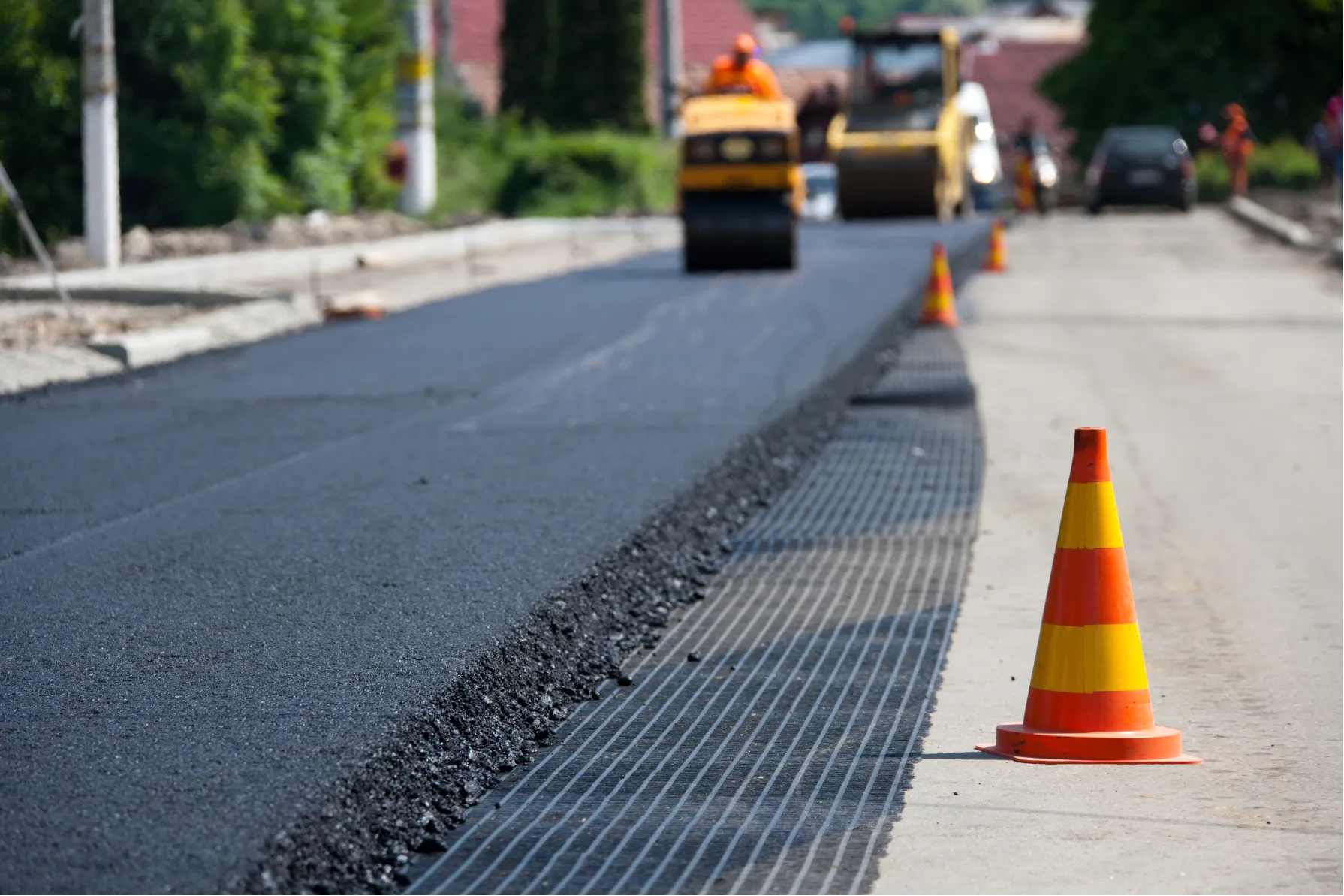 overlays-h Fresh asphalt being laid on a road, with traffic cones marking the construction area.