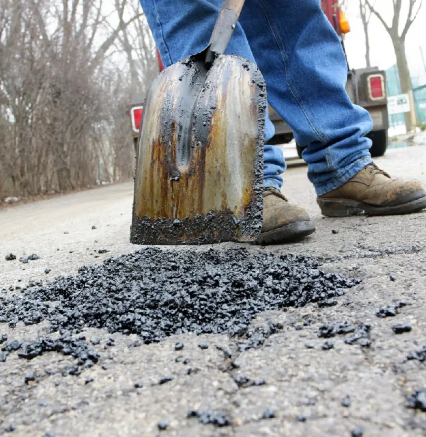 crackfilling-3 Close-up of a person shoveling asphalt to fill a pothole on a cracked road.