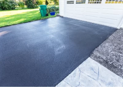 Freshly paved black asphalt driveway in front of a white garage, completed by Jones Asphalt VA Expert Asphalt Services, with green grass and bins nearby.