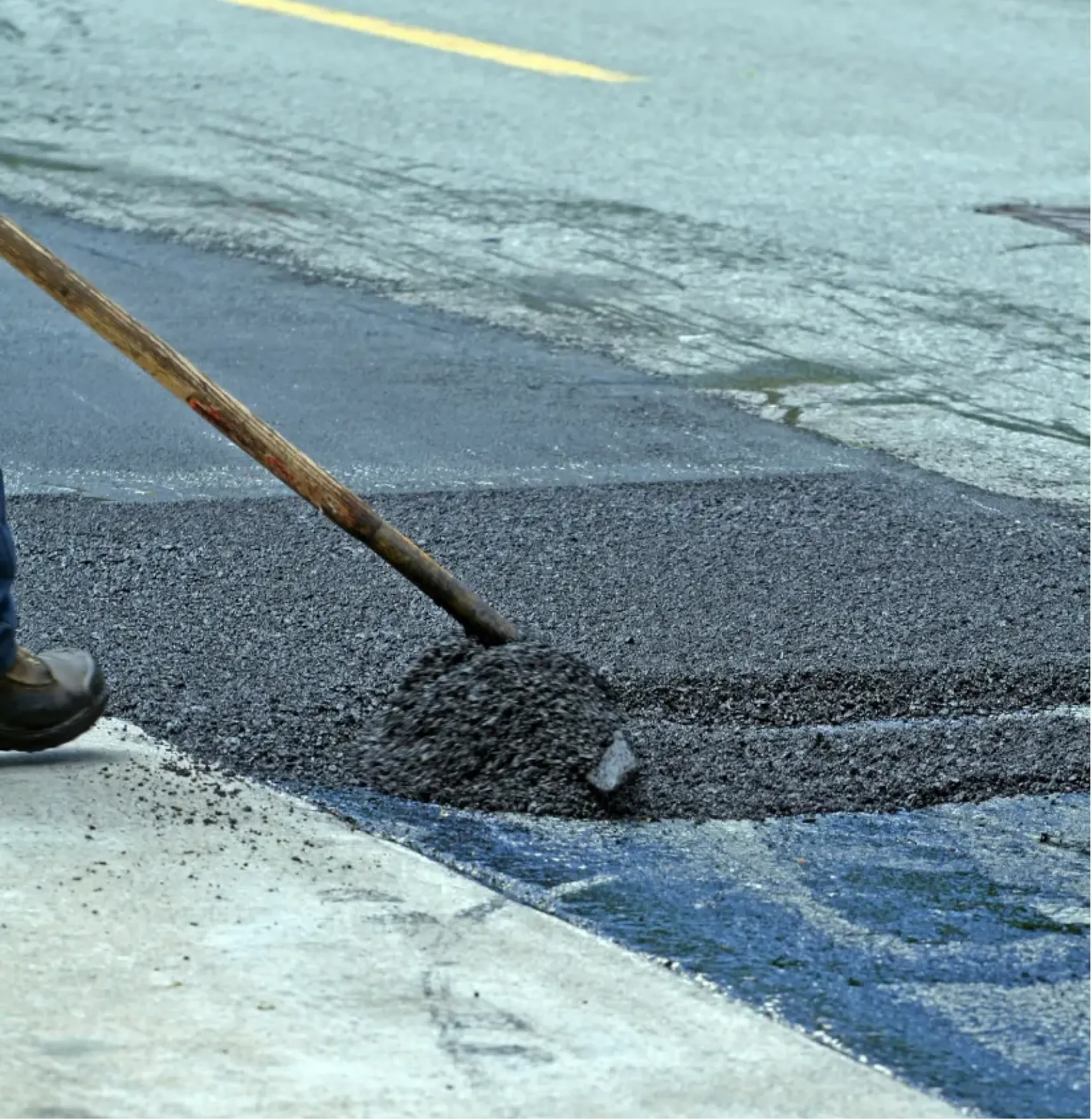 pothole-3 A worker spreads fresh asphalt on a cracked road using a shovel.
