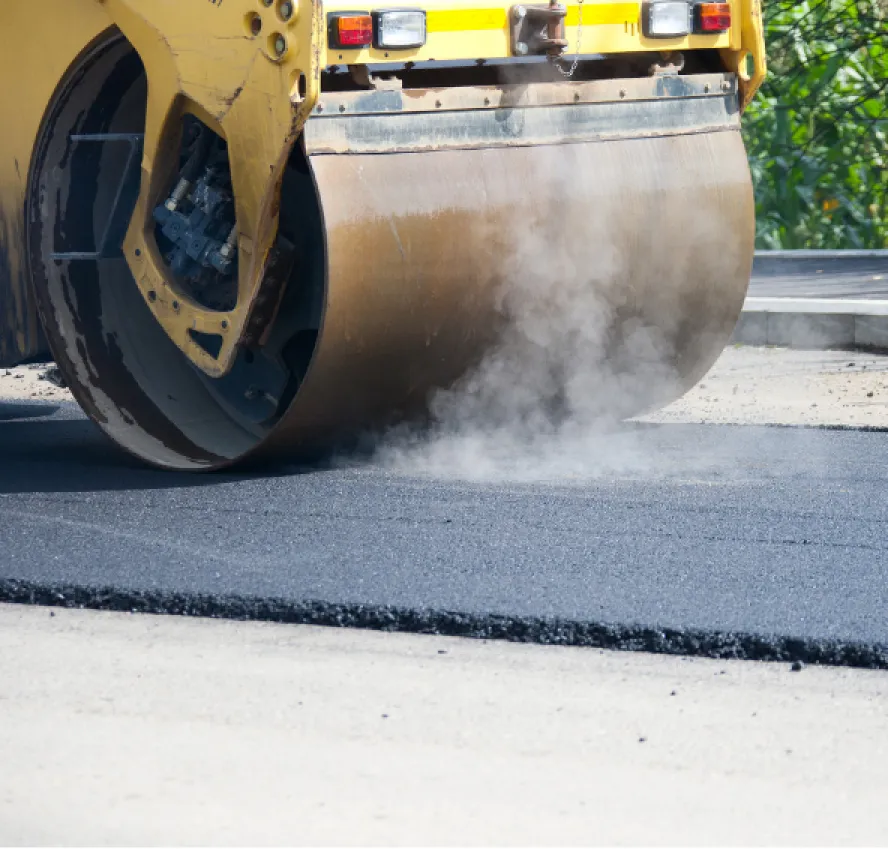A steamroller compressing hot asphalt on a road under construction, with steam rising from the surface.