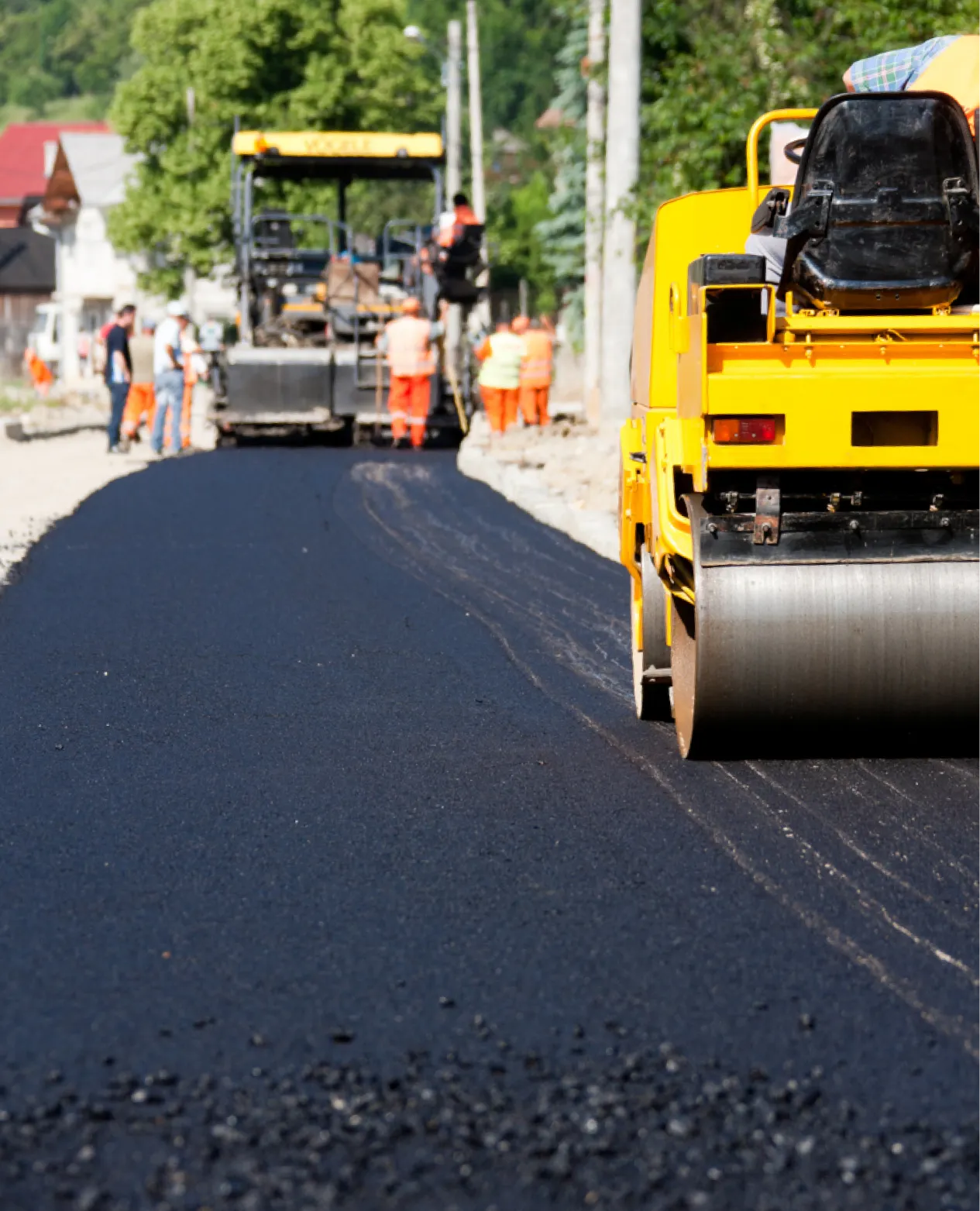 why-choose-1 Workers and machinery paving a new asphalt road on a sunny day in a residential area.